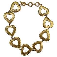 YVES SAINT LAURENT vintage gold tone necklace featuring massive textured heart links and a heart link embossed with the YVES SAINT LAURENT cursive signature. Adjustable toggle clasp. Embossed with cursive YVES SAINT LAURENT signatures on the heart toggles. Made in France. Indicative measurements : adjustable length from approx. 44 cm (17.32 inches) to approx. 49 cm (19.29 inches) / width of the heart links approx. 3.7 cm (1.46 inches). Material : Gold tone metal hardware. NOTES - This is a preloved vintage item, therefore it might have imperfections. - Colors may differ slightly from actual product appearance due to differences in lighting conditions. - As a buyer, you are fully responsible for customs duties, other local taxes and any administrative procedures related to imports into the Cursive Signature, Saint Laurent Vintage, Work Necklaces, Diamond Tennis Necklace, Triangle Necklace, Tennis Necklace, Gold Tone Necklace, Cross Designs, Toggle Clasp