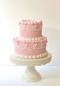 a three tiered cake with pink icing and flowers on top is sitting on a white pedestal