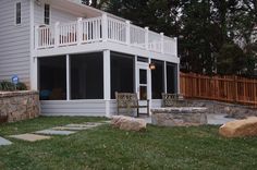 a house with a deck and patio in the front yard, next to a rock wall