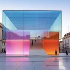 people are walking around in front of a building with colorful glass panels on the side