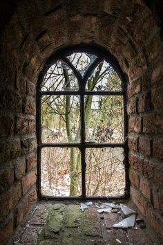 an open window in the side of a brick wall looking out at trees and snow