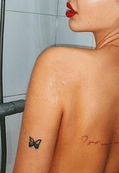 a woman with a butterfly tattoo on her upper arm and shoulder, standing in front of a shower