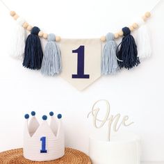 a first birthday banner with tassels hanging from it's sides and a cake in the foreground