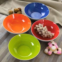 four bowls with different colors and designs on them, sitting on a wooden floor next to some nuts