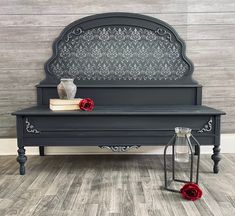 a black bench sitting on top of a wooden floor next to a vase with flowers