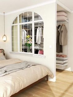 a bedroom with a bed, closet and clothes hanging on the wall in front of an open window