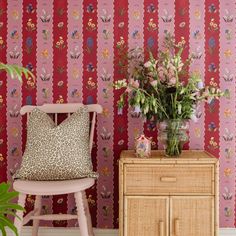 a pink wallpapered room with a chair, vase and flowers on the table