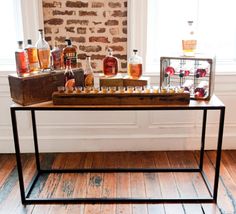 a wooden table topped with bottles of alcohol on top of a hard wood floor next to a window