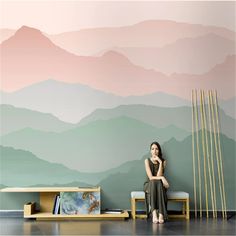 a woman sitting on a bench in front of a wall with mountains painted on it