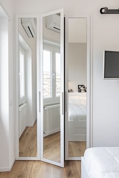 a bedroom with white walls and wooden floors has a large mirror on the wall next to the bed