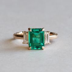 Lab grown emerald adorned with baguette diamondsCut: EmeraldThree stone ringStone Size: 8 x6 mmBaguette Diamonds: Two 4.5 x 2 mmDiamond Clarity: SIDiamond Color: GHIDiamond weight: 0.12 carat eachTotal Diamond Weight: 0.25 caratMetal Type: 18 karat gold Emerald Gold Ring Vintage, Emerald 3 Stone Ring, Three Stone Emerald Ring, Emerald Ring Vintage Gold, Art Deco Emerald Engagement Ring, Diamond Ring With Emerald Accents, Emerald Cut Emerald Engagement Ring, Emerald Stone Engagement Ring, Diamond And Emerald Engagement Ring