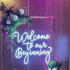 a neon sign that says welcome to our beginning with flowers and greenery around it