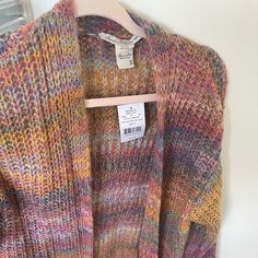 a multicolored cardigan sweater hanging on a hanger next to a white wall