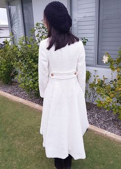 a woman standing in front of a house wearing a white coat and black booties