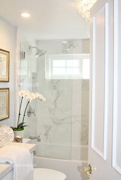 a white bathroom with marble counter tops and walls, along with framed pictures on the wall