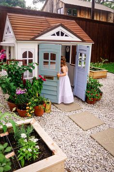 a woman in a white dress standing outside of a blue and white shed with flowers