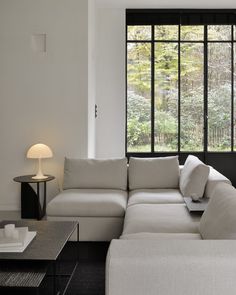 a large white couch sitting in front of a window next to a table with a lamp on it