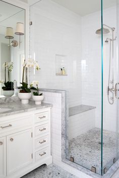 a white bathroom with marble counter tops and glass shower doors, along with two vases filled with flowers