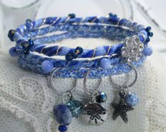 three bracelets with charms and beads on top of a white lace table cloth,