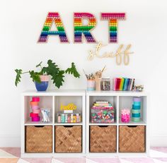 a white shelf with baskets and craft supplies on it in front of a wall that says art stuff