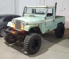 an old green jeep is parked in a garage