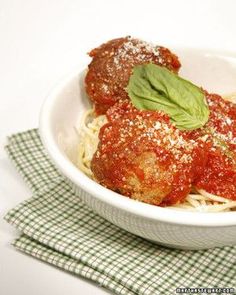 spaghetti and meatballs are served in a white bowl on a green checkered napkin