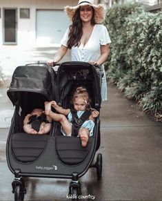 a woman pushing a stroller with two babies in it and another child sitting in the stroller