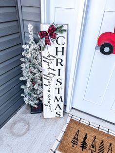 a christmas sign sitting on the front porch next to a tree and potted plant