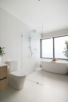 a white bathroom with a tub, toilet and sink next to a large window that looks out onto the ocean