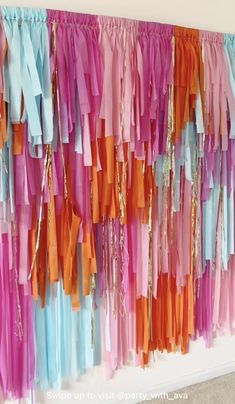 colorful streamers are hanging on the wall in front of a white wall with an orange, pink, and blue backdrop