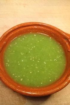 a bowl filled with green soup sitting on top of a wooden table next to a spoon