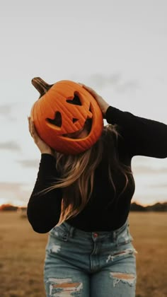 a woman in ripped jeans holding up a pumpkin with her face carved into the shape of a jack - o'- lantern