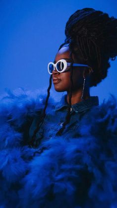 a woman wearing large white sunglasses and blue feathers