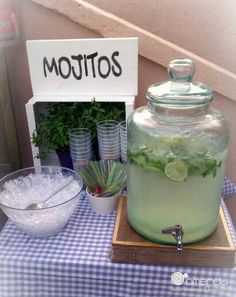 a table topped with a large glass jar filled with ice and limes next to a bowl of food