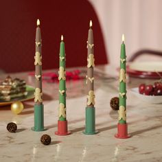 four candles are sitting on a table with pine cones and other holiday decorations around them