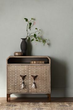 a wooden cabinet with two vases on top of it next to a flower pot