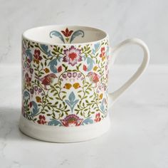 a coffee cup decorated with flowers and leaves on a marble table top, ready to be used as a mug