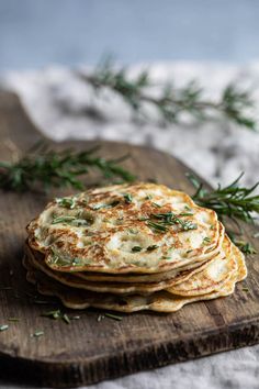 a wooden cutting board topped with pancakes covered in cheese and herbs