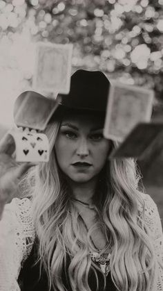 a woman with long blonde hair wearing a hat and holding cards in front of her face