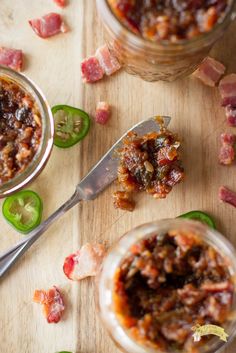 two jars filled with food sitting on top of a wooden table next to green peppers