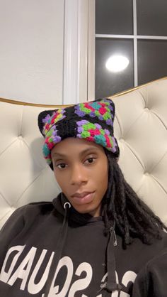 a woman sitting in a chair wearing a black hoodie with colorful crochet on it