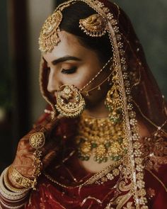 a woman in a red and gold bridal outfit with jewelry on her head, looking down