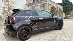 a black sports car parked in front of an old building with graffiti on the side