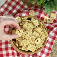 a person reaching for crackers in a bowl on a checkered table cloth next to a potted plant