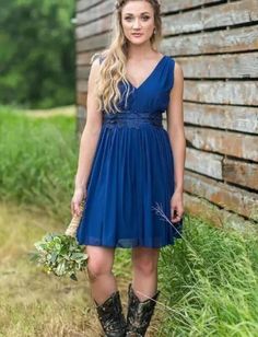 a beautiful young woman standing in front of a barn wearing a blue dress and cowboy boots