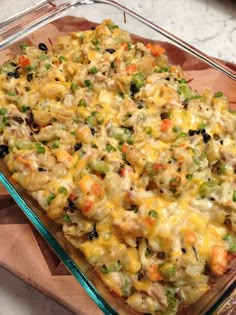 a casserole dish with chicken and vegetables in it sitting on a wooden cutting board