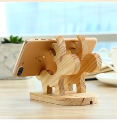 a wooden phone holder with two elephants on it's sides and a coffee cup in the background