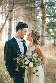 a bride and groom are standing in the woods with flowers on their heads, looking into each others eyes