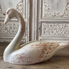 a white swan sitting on top of a wooden floor next to a wall with ornate carvings