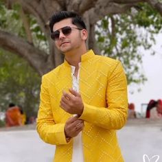 a man in a yellow jacket and sunglasses standing next to a tree with his hands folded